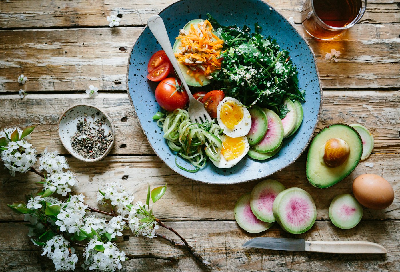 Bol de salade composée avec œuf, avocat et courgettes, posé sur une table en bois